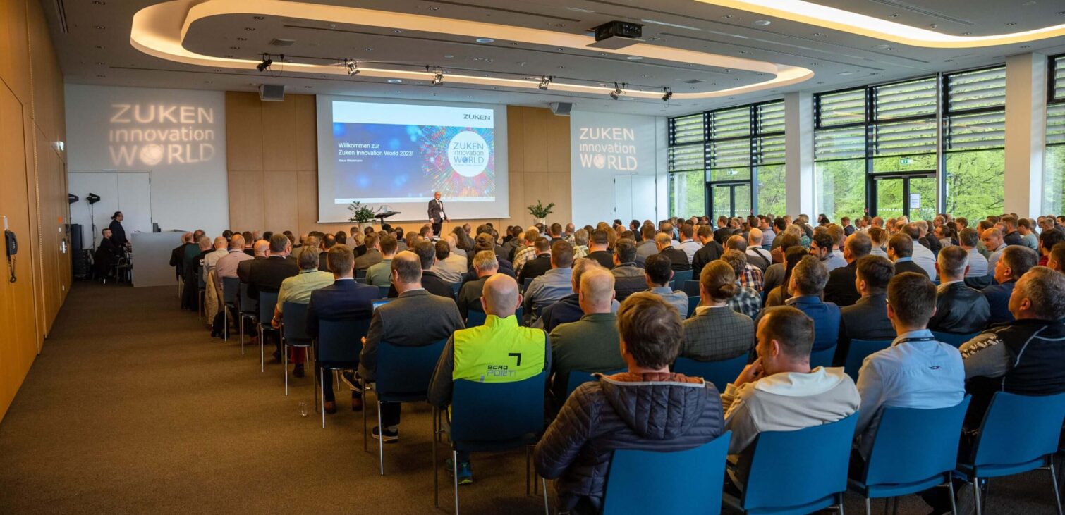 Attendees seated in a conference room facing a presentation screen with 'ZUKEN Innovation World' prominently displayed, indicating a professional event with a focus on technological innovations and industry advancements