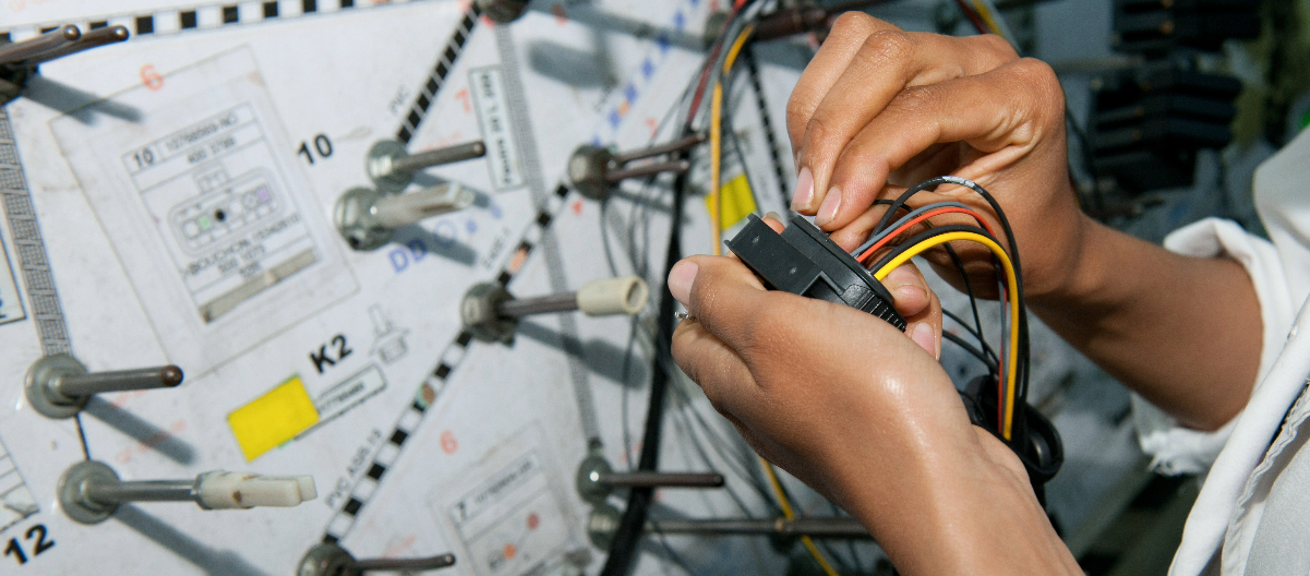Close-up view of assembling a colorful wire harness, with focused attention to detail, against a backdrop of a wire harness manufacturing diagram, highlighting the precision required in this intricate work.
